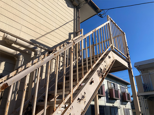 経年劣化により激しく錆び、塗装が剥がれ落ちたアパートの屋外鉄骨階段のクローズアップ。